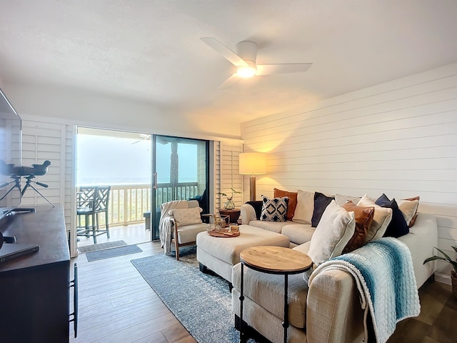 living room with hardwood / wood-style flooring, ceiling fan, and wooden walls