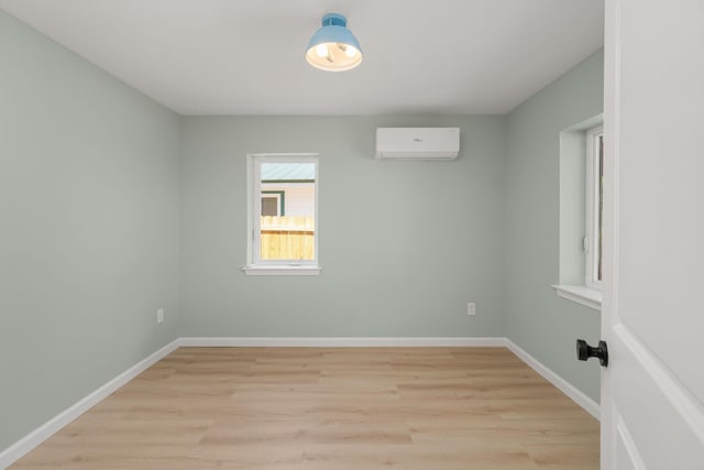 spare room featuring a wall mounted AC, light wood-style flooring, and baseboards