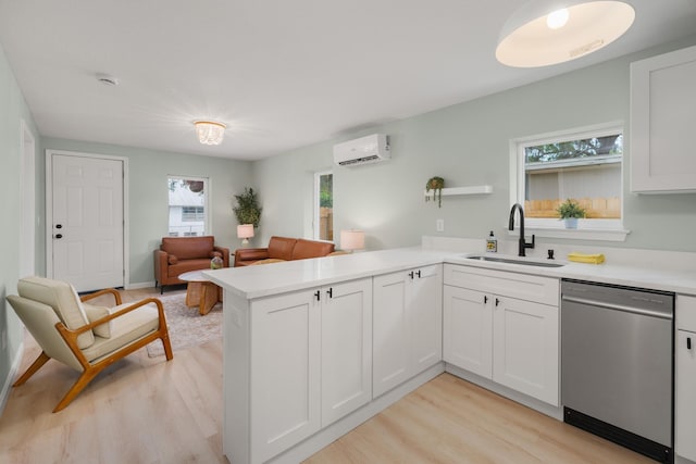 kitchen with dishwasher, a sink, a wall unit AC, light wood-style flooring, and a peninsula