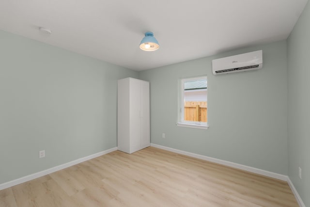 spare room featuring a wall unit AC, light wood-style flooring, baseboards, and a smoke detector