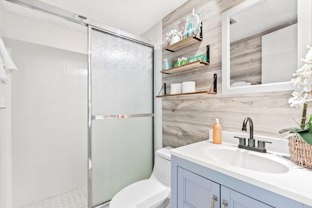 bathroom featuring vanity, wood walls, a shower with door, toilet, and a textured ceiling