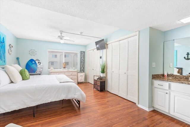 bedroom featuring ceiling fan, wood-type flooring, a textured ceiling, and two closets