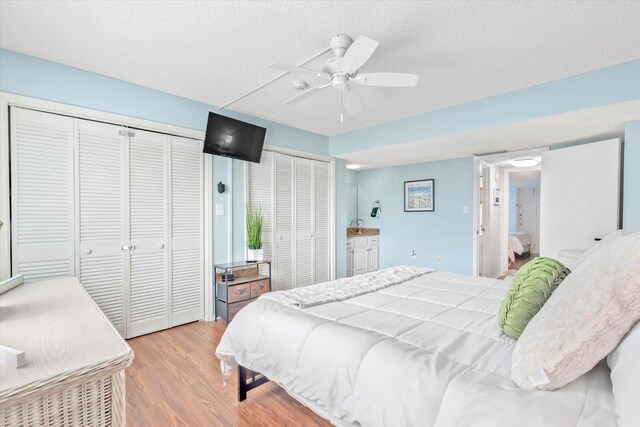 bedroom featuring ensuite bathroom, ceiling fan, a textured ceiling, light hardwood / wood-style floors, and multiple closets