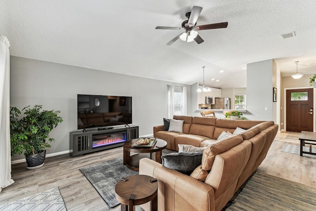 living room featuring light wood-style floors, vaulted ceiling, a ceiling fan, a textured ceiling, and baseboards