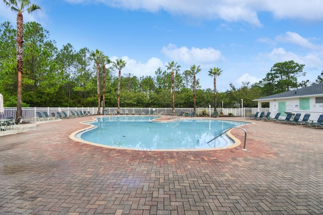 community pool featuring fence, view of scattered trees, and a patio area
