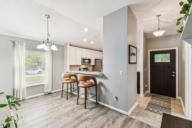 foyer entrance with baseboards, a chandelier, light wood finished floors, recessed lighting, and a textured ceiling