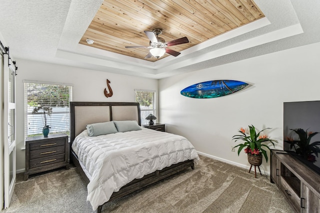 bedroom with a raised ceiling, carpet, baseboards, a barn door, and a ceiling fan