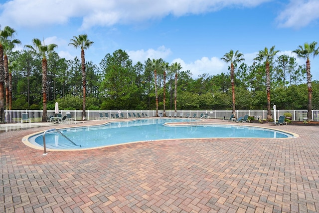 community pool featuring fence, a patio area, and view of wooded area