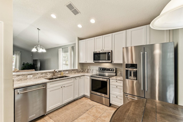 kitchen with appliances with stainless steel finishes, a sink, healthy amount of natural light, white cabinets, and vaulted ceiling