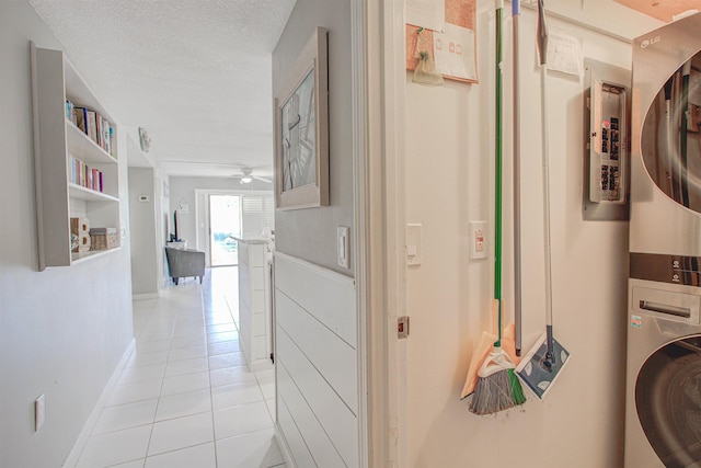 washroom with ceiling fan, stacked washer and dryer, light tile patterned floors, and a textured ceiling