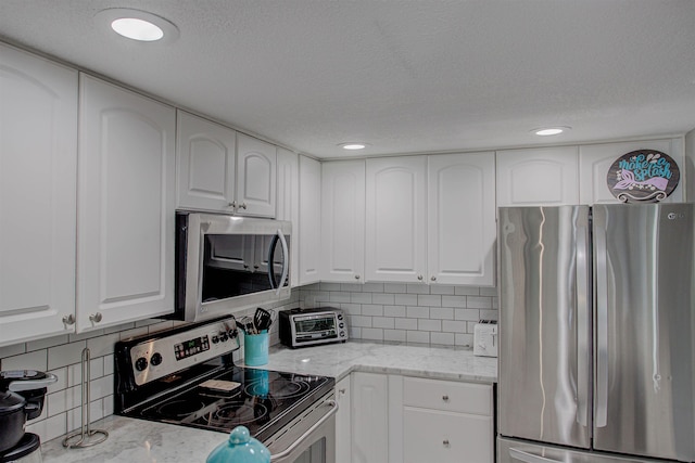 kitchen featuring white cabinets, decorative backsplash, light stone counters, and appliances with stainless steel finishes