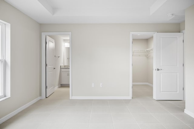 unfurnished bedroom featuring connected bathroom, a walk in closet, light tile patterned floors, a raised ceiling, and a closet