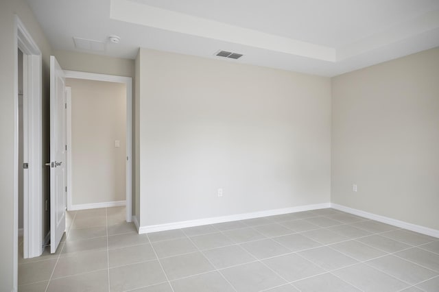 tiled empty room featuring a raised ceiling