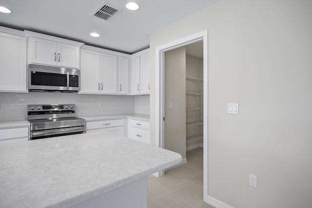 kitchen with tasteful backsplash, appliances with stainless steel finishes, light tile patterned floors, and white cabinets