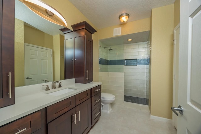 bathroom featuring vanity, a textured ceiling, tiled shower, toilet, and tile patterned floors