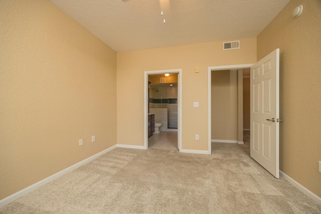 unfurnished bedroom featuring a textured ceiling, connected bathroom, and light colored carpet