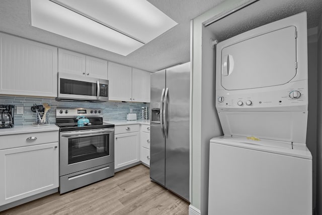 kitchen with stacked washer and clothes dryer, white cabinetry, appliances with stainless steel finishes, light hardwood / wood-style floors, and decorative backsplash