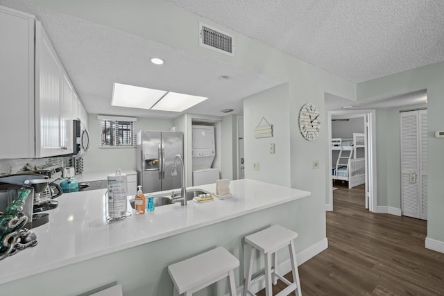 kitchen with stainless steel appliances, white cabinetry, stacked washer and clothes dryer, and kitchen peninsula