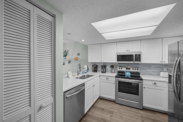 kitchen with appliances with stainless steel finishes, sink, backsplash, white cabinets, and light hardwood / wood-style floors