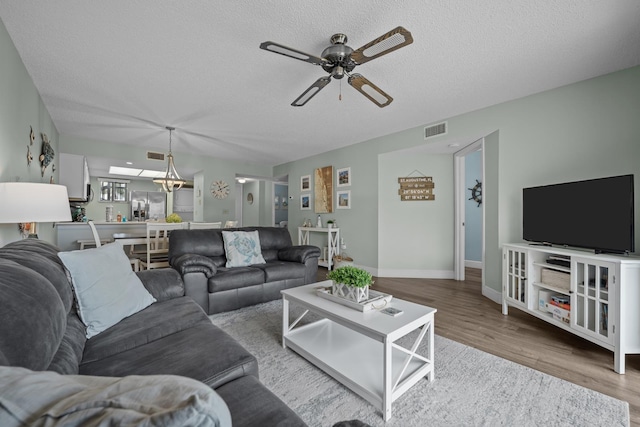 living room with hardwood / wood-style floors, ceiling fan with notable chandelier, and a textured ceiling