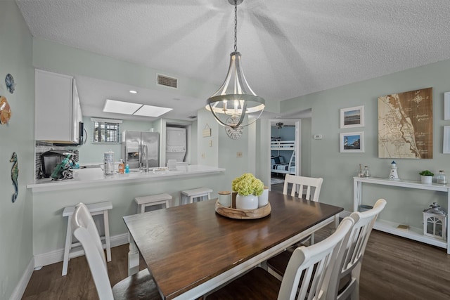 dining space featuring dark hardwood / wood-style flooring, a skylight, a chandelier, and a textured ceiling