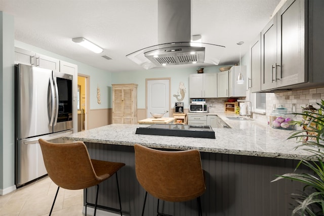 209 Alerto St, Saint Augustine, FL 32080 - kitchen with stainless steel appliances, a peninsula, island exhaust hood, tasteful backsplash, and light stone countertops
