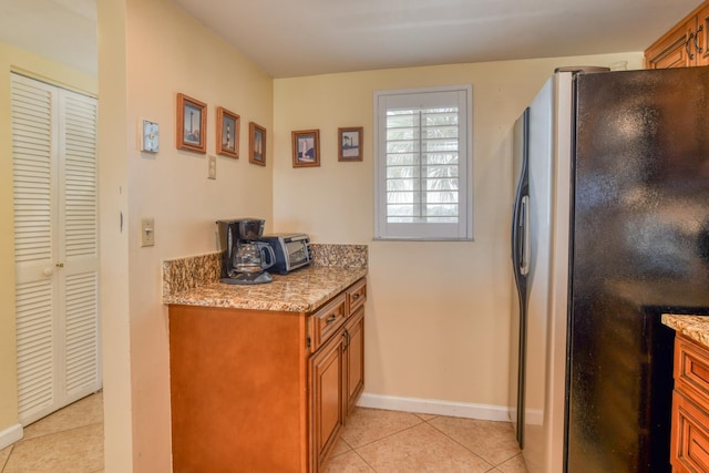 kitchen featuring stainless steel fridge, light tile patterned flooring, and light stone counters