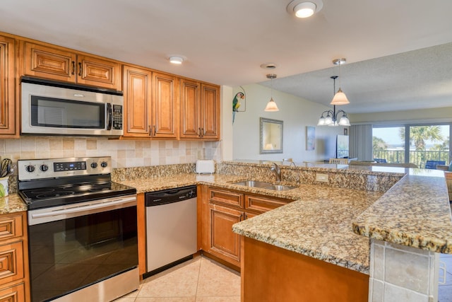 kitchen featuring light stone countertops, sink, hanging light fixtures, stainless steel appliances, and decorative backsplash