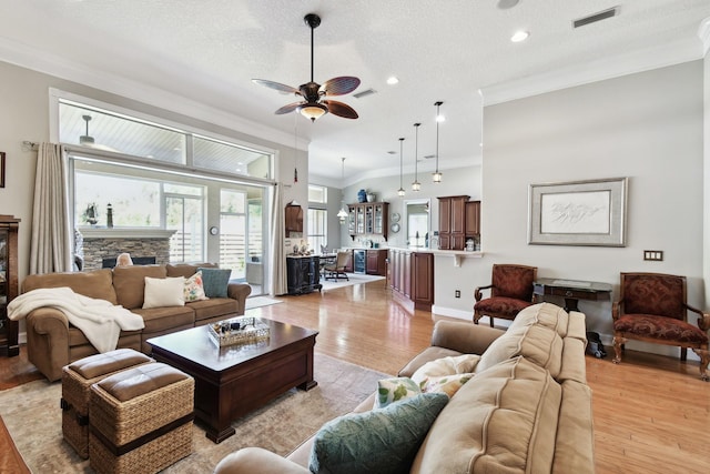 living room with a textured ceiling, light hardwood / wood-style flooring, ceiling fan, and ornamental molding