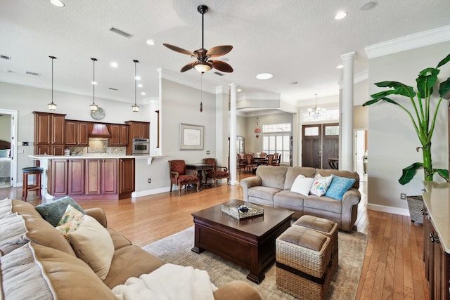 living room with ornate columns, light hardwood / wood-style flooring, a textured ceiling, ceiling fan with notable chandelier, and ornamental molding