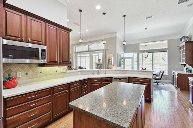 kitchen featuring a center island, light hardwood / wood-style flooring, crown molding, a textured ceiling, and appliances with stainless steel finishes