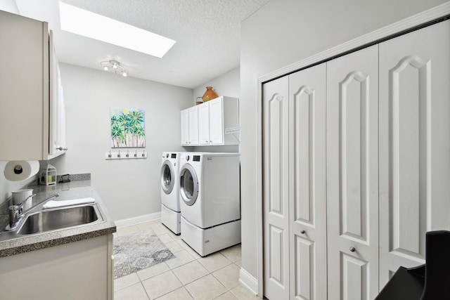 laundry room with a skylight, sink, cabinets, washing machine and dryer, and light tile patterned flooring