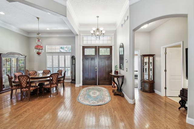 entrance foyer with a notable chandelier, crown molding, a towering ceiling, a textured ceiling, and light wood-type flooring