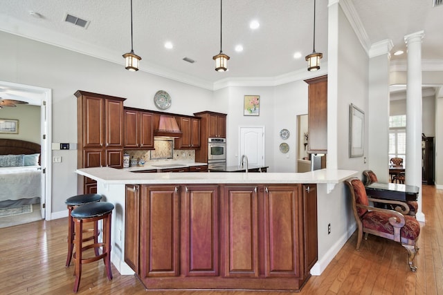 kitchen featuring crown molding, light wood-type flooring, hanging light fixtures, and premium range hood