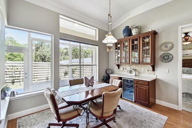 dining room with wine cooler, ornamental molding, and light wood-type flooring