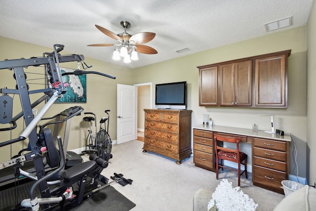 workout room featuring a textured ceiling, ceiling fan, and light carpet