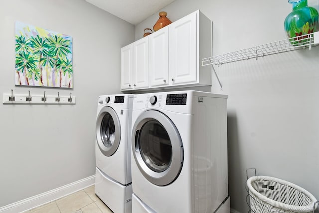 clothes washing area featuring washing machine and clothes dryer, light tile patterned flooring, and cabinets