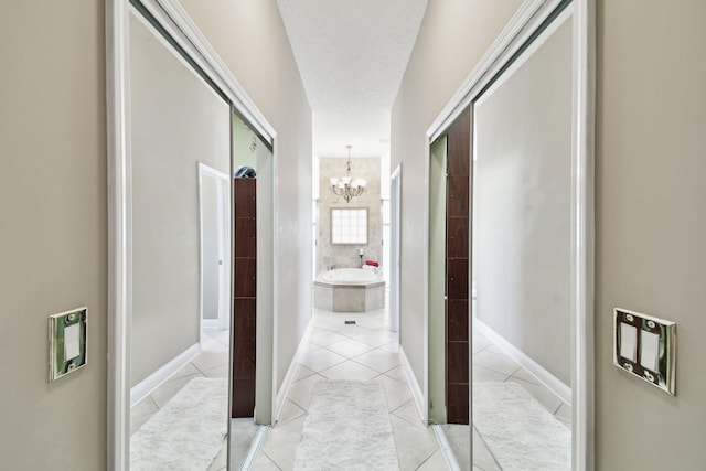 corridor with light tile patterned floors, a textured ceiling, and an inviting chandelier