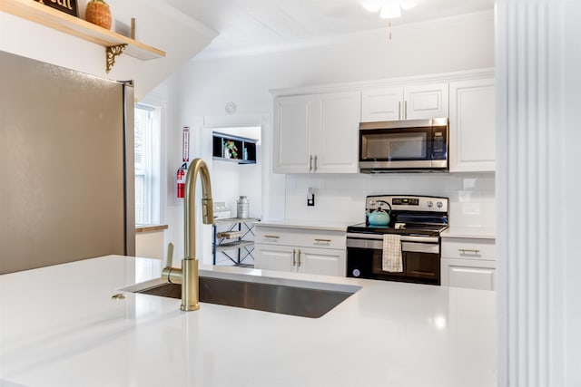kitchen with backsplash, light countertops, stainless steel appliances, white cabinetry, and a sink