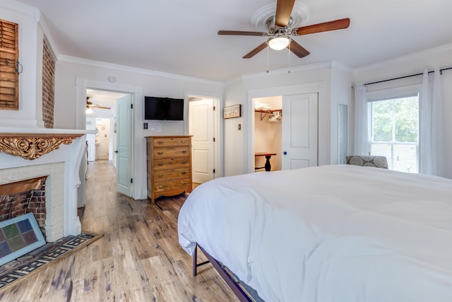 bedroom featuring a brick fireplace, ceiling fan, crown molding, hardwood / wood-style flooring, and a closet