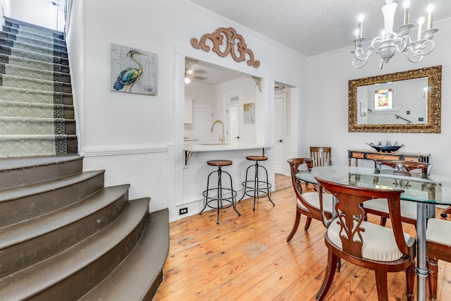 dining area featuring sink, a chandelier, a textured ceiling, light wood-type flooring, and ornamental molding