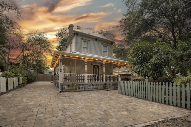 view of front facade with a fenced front yard, covered porch, a chimney, and metal roof