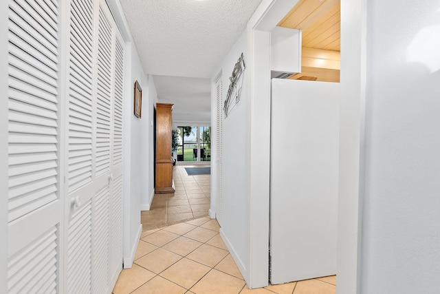 hall with light tile patterned flooring, a textured ceiling, and baseboards