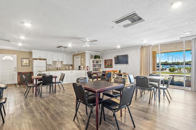 dining space featuring crown molding, a textured ceiling, light wood-style flooring, and ceiling fan