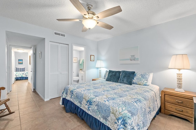 bedroom featuring a textured ceiling, light tile patterned flooring, a closet, ensuite bathroom, and ceiling fan