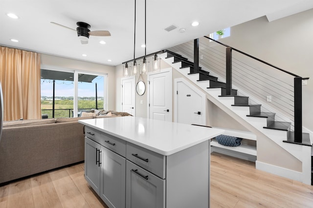 kitchen with gray cabinets, ceiling fan, hanging light fixtures, a kitchen island, and light wood-type flooring