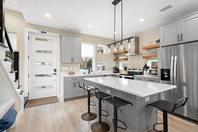 kitchen featuring wall chimney range hood, a kitchen breakfast bar, stainless steel appliances, a center island, and light hardwood / wood-style floors