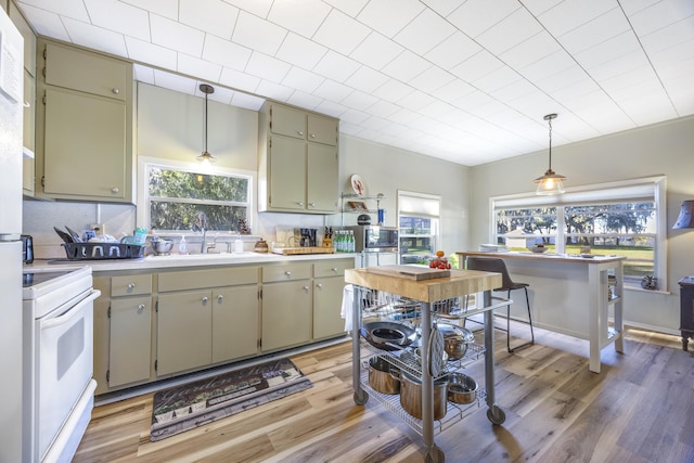 kitchen with white electric range, light hardwood / wood-style floors, pendant lighting, and sink