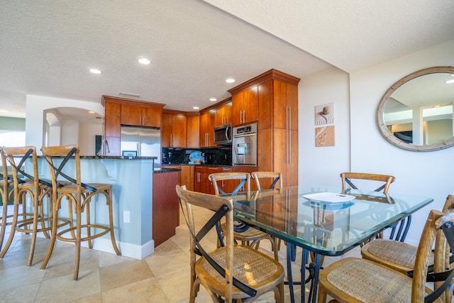 kitchen featuring a textured ceiling, backsplash, light tile patterned floors, and stainless steel appliances