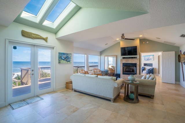 living room featuring a textured ceiling, vaulted ceiling, ceiling fan, a water view, and a tiled fireplace